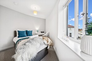 Un dormitorio con cama, mesita de noche, lámpara, ventana con vistas y una planta.