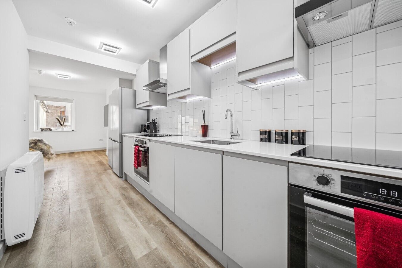 Een moderne keuken met witte kasten, een ingebouwde oven, een vaatwasser en een raam met uitzicht op een bakstenen gebouw.