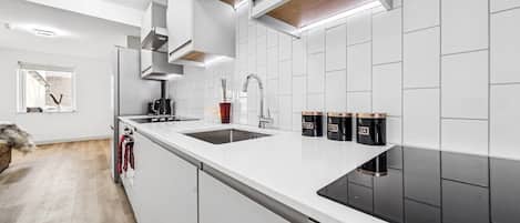 A modern kitchen with white cabinetry, a black stovetop, and a window with a view.