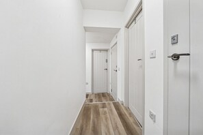 Un couloir étroit aux murs blancs et au plancher en bois, qui mène à une porte dotée d’une poignée et d’une serrure.