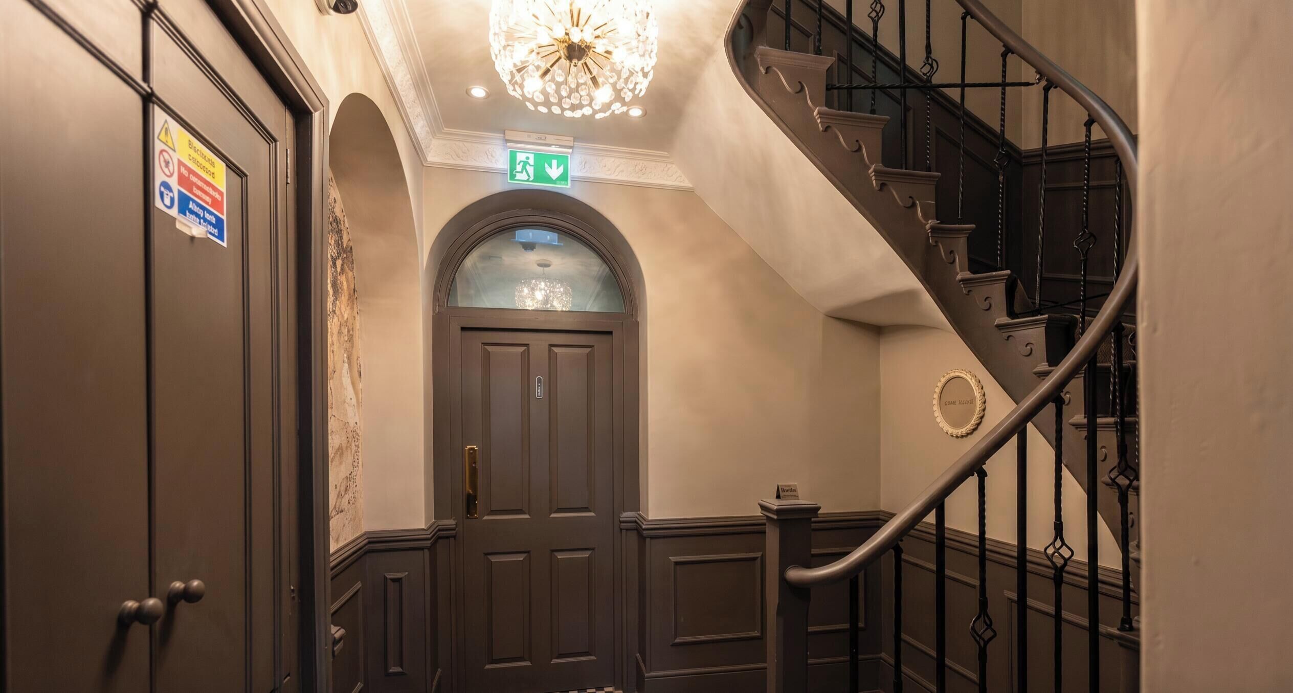 Ein Hotelinneres mit einer imposanten Treppe, einer Tür mit Schild und einem Kronleuchter.