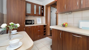 A modern kitchen with wooden cabinets, a microwave, and a fruit bowl on the counter. - Spacious Apartment with Balcony | 3 Bedrooms | Workspace (Zabrze)
