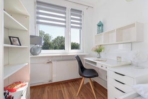 Une pièce moderne et bien éclairée, avec un bureau blanc, une chaise noire et un radiateur.
