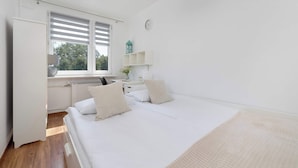 A bedroom with a bed, a desk, a radiator, a window with blinds, and a clock on the wall. - Spacious Apartment with Balcony | 3 Bedrooms | Workspace (Zabrze)