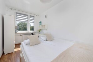 Une chambre à coucher avec un lit, un bureau, un radiateur, une fenêtre avec des stores et une horloge au mur.