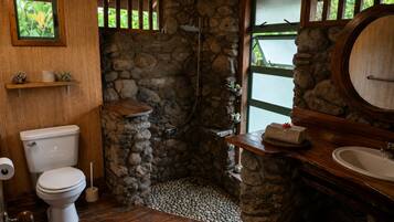 A bathroom with a stone shower enclosure, a toilet, a sink, and a window with a view.