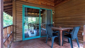 Een houten terras met een glazen deur die uitkomt op een buitenruimte met een tafel en stoelen.