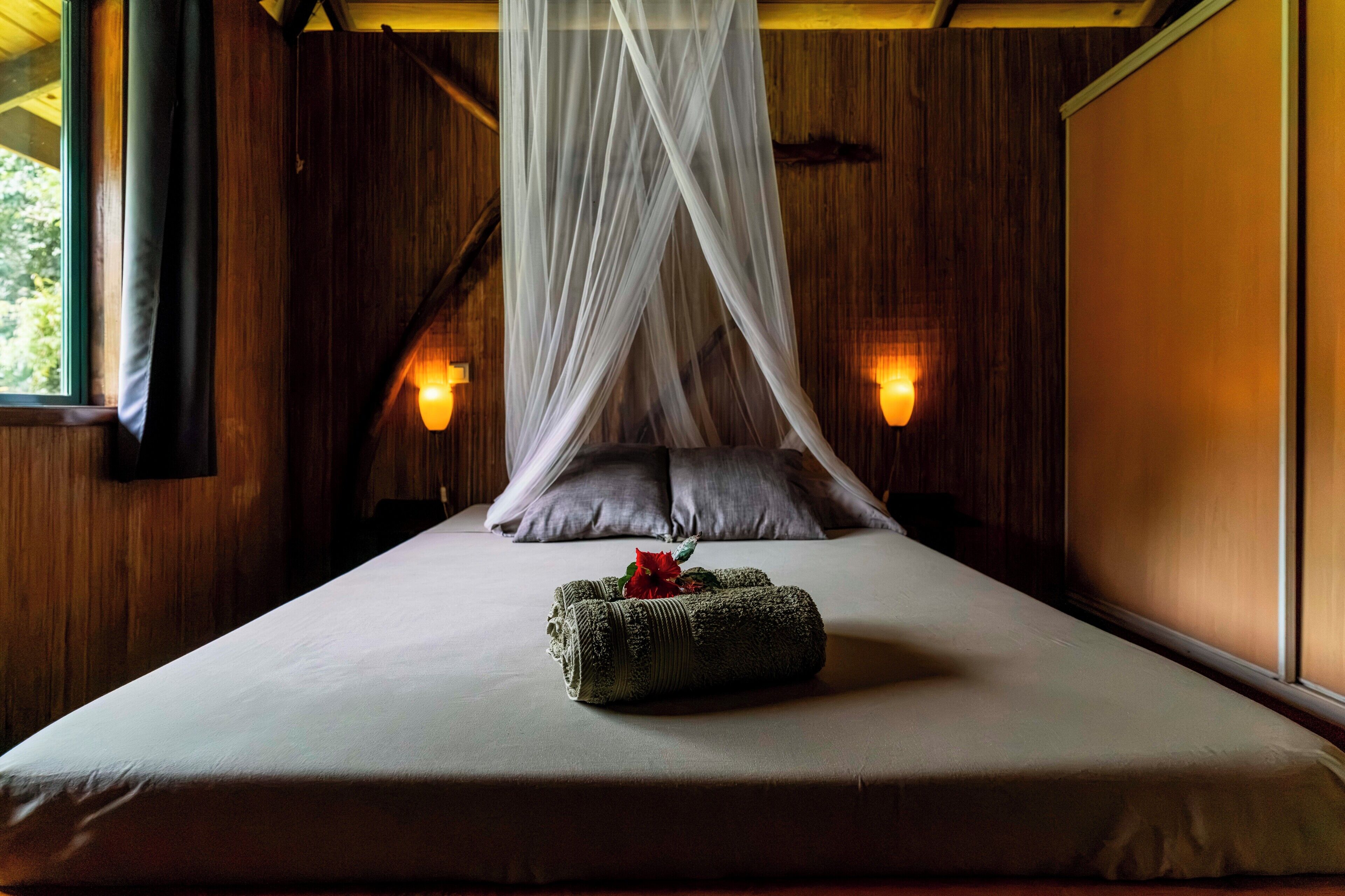 A bed with a canopy, pillows, a bedside lamp, and a decorative pillow with a flower.