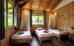 Una habitación de madera con tres camas, cada una con dosel, y un ventanal grande.