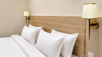 A neatly made bed with white linens and pillows, a wooden headboard, and two wall-mounted lamps with gold accents.