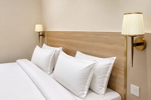 A neatly made bed with white linens and pillows, a wooden headboard, and two wall-mounted lamps with gold accents. - Hotel SEZ Park by Divoy Hotels & Resorts (Jaipur)