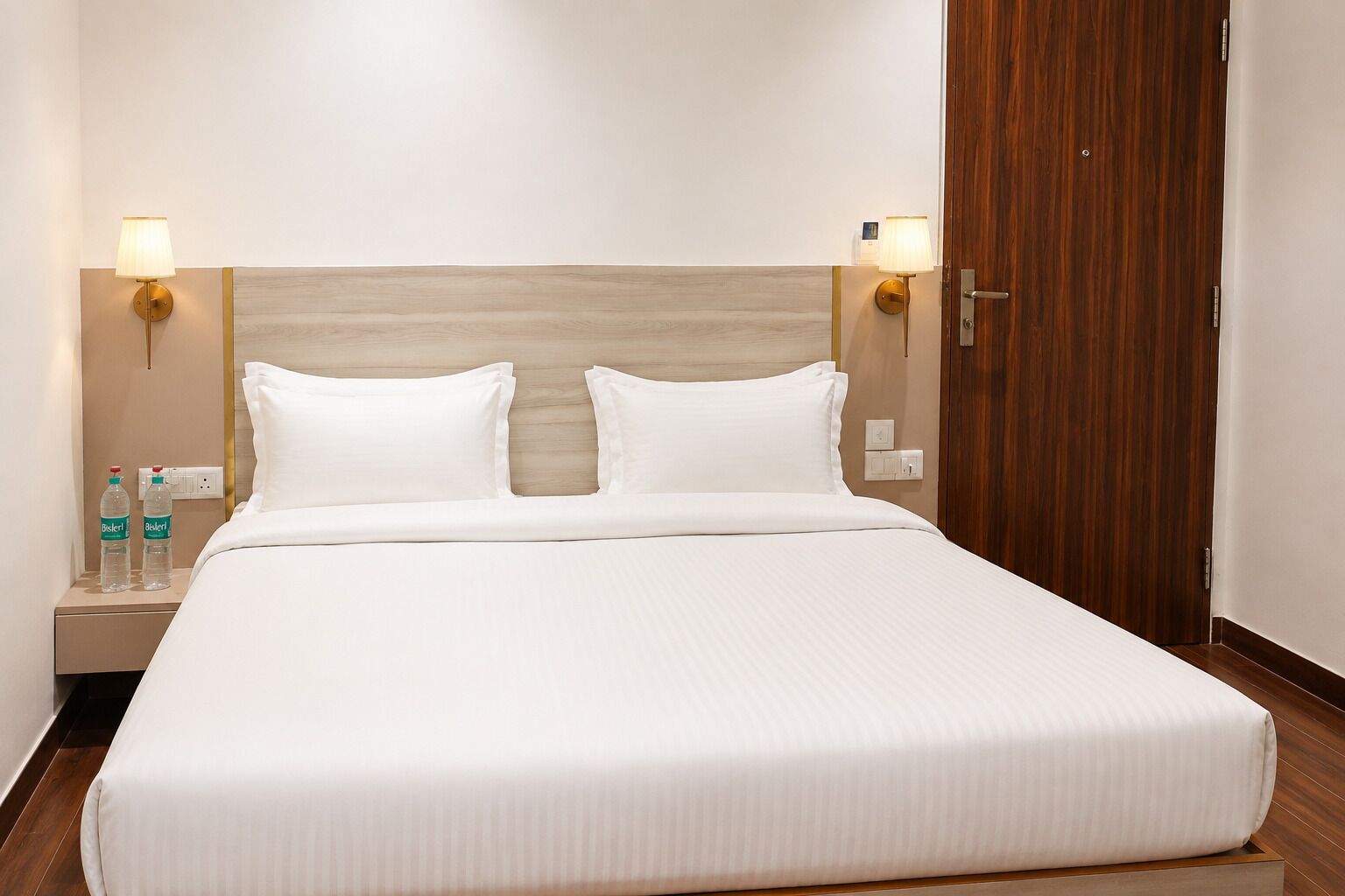 Una habitación de hotel con una cama grande, dos lámparas de noche, un cabecero de madera y un armario de madera.