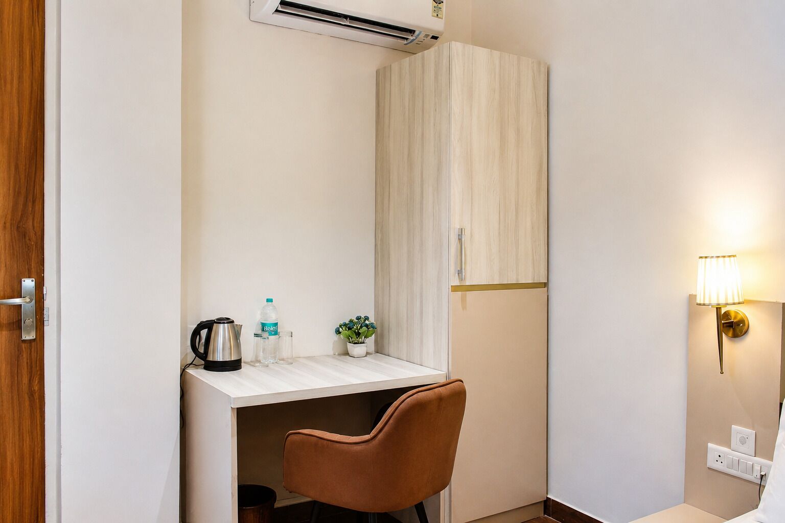 Ein kleines Zimmer mit Küchenzeile, einem braunen Sessel, einem kleinen Tisch mit Wasserkocher, einer Flasche und einer Pflanze.