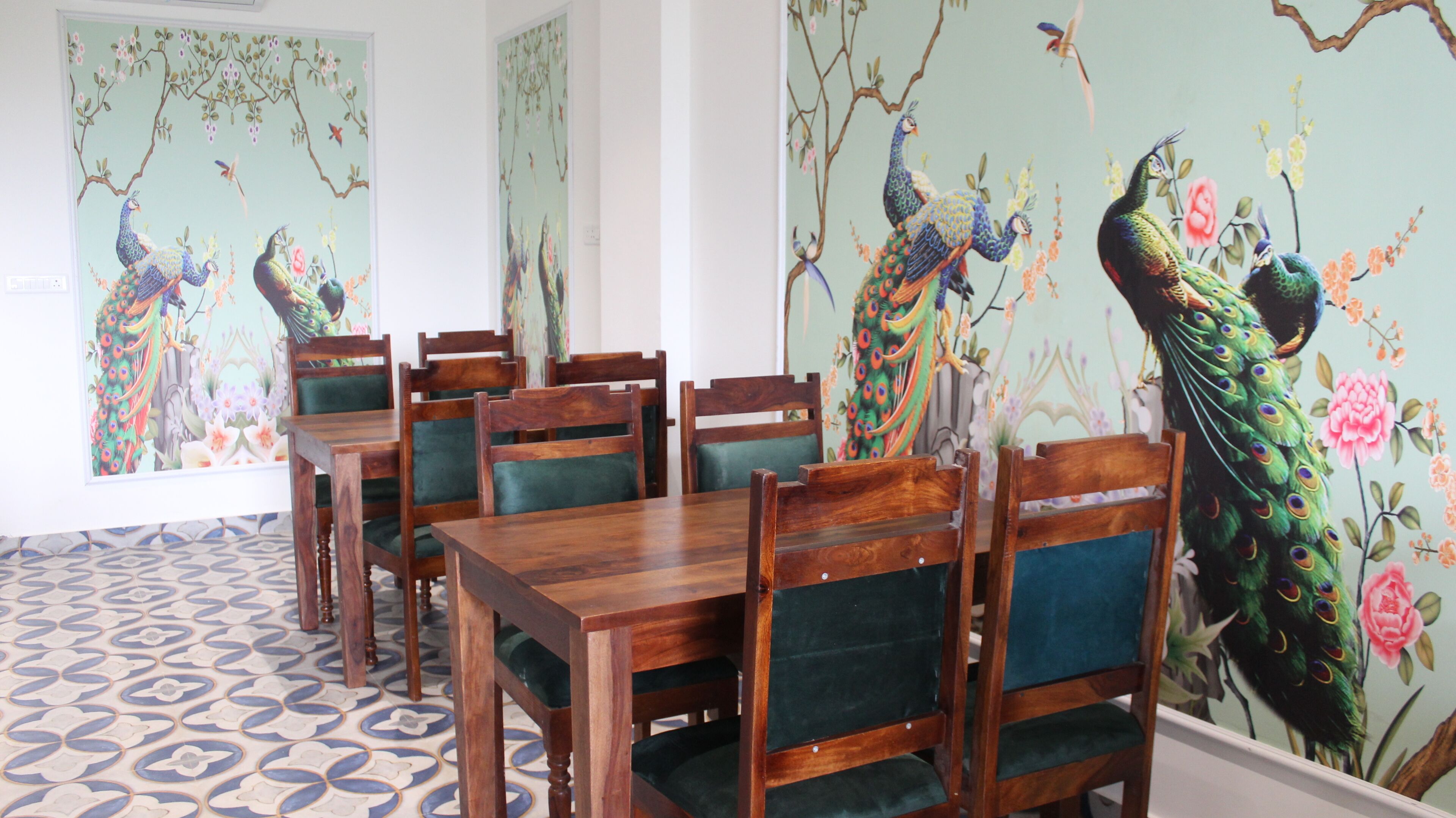 Un comedor con mesas y sillas de madera, rodeado de paredes con pinturas murales de pavos reales.
