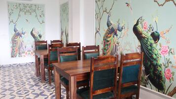 Un comedor con mesas y sillas de madera, rodeado de paredes con pinturas murales de pavos reales.