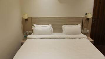 A hotel room with a bed, two bedside lamps, a nightstand with water bottles, and a wooden headboard.