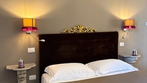 Habitación de hotel con una cama grande, dos lámparas de pared, una mesita de noche pequeña y un cabecero decorativo.