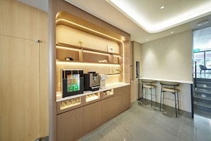 A modern kitchenette with a built-in coffee machine, a refrigerator, and a bar area with stools. - Howard Residence (Taipei)