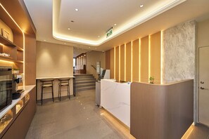 A modern reception area with a counter, seating, and a staircase leading to an upper level. - Howard Residence (Taipei)
