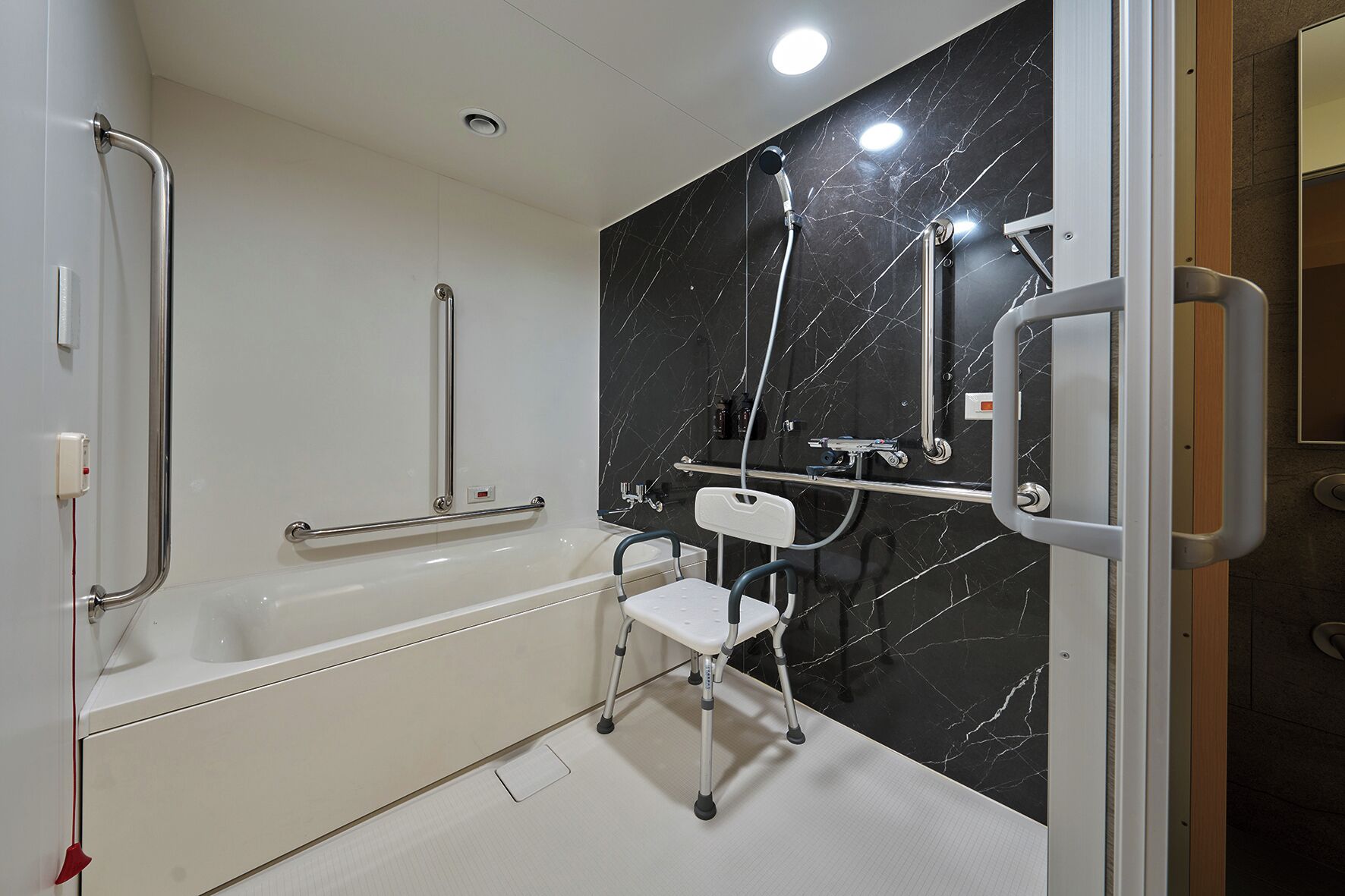 A bathroom with a white bathtub, a shower with a handheld showerhead, and a grab bar.