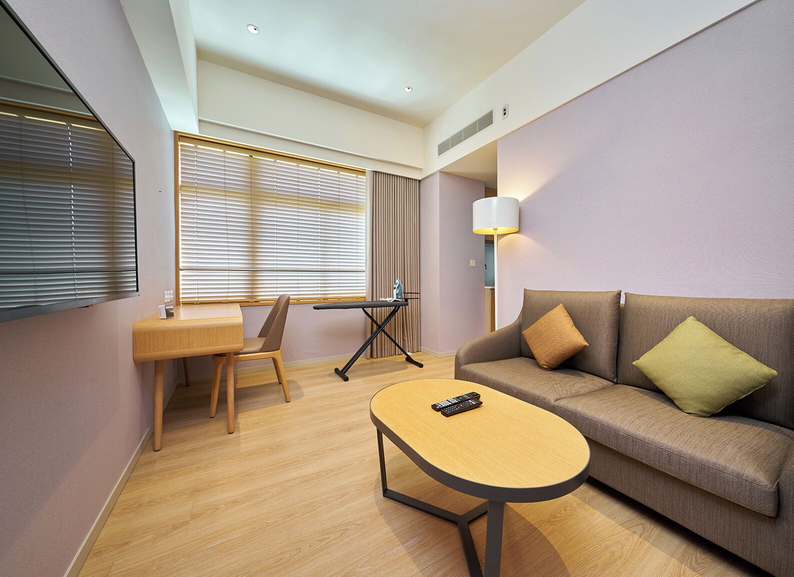 Una habitación de hotel con un escritorio de madera, un sofá, una lámpara y un control remoto sobre una mesita.