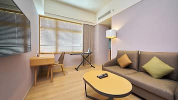Una habitación de hotel con un escritorio de madera, un sofá, una lámpara y un control remoto sobre una mesita.