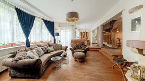 A spacious living room with a large sofa, a smaller armchair, and a coffee table. A staircase leads to an upper level, and a piano is visible in the background. - Apartamenty Sun & Snow Villa Łokietka (Sopot)