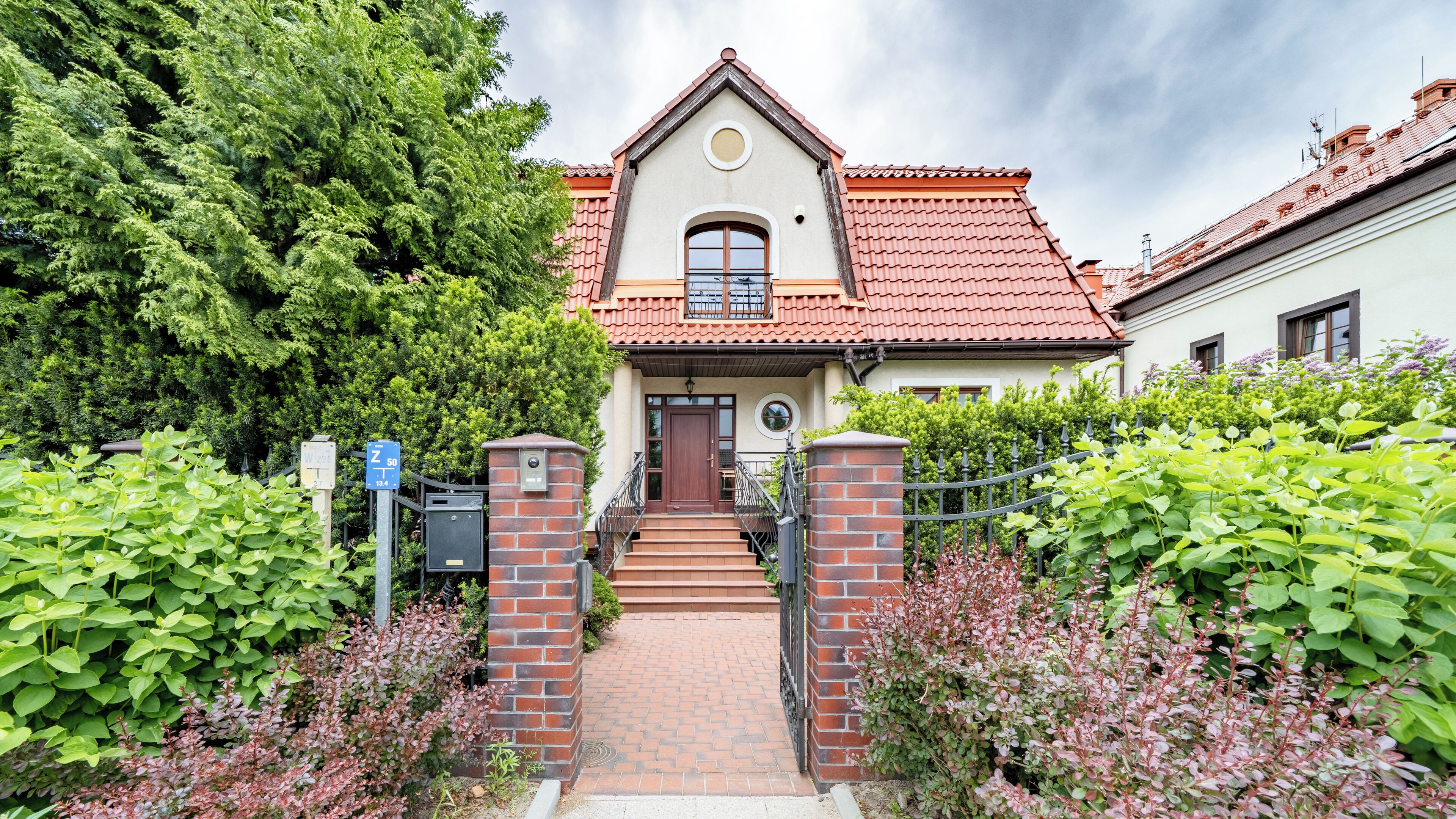 A two-story house with a red-tiled roof, a front door, and a small balcony.
