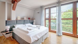 A modern bedroom with a large bed, a bedside table, a lamp, and a view of greenery through the window. - Apartamenty Sun & Snow Villa Łokietka (Sopot)