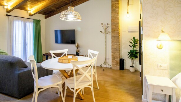 Ein gemütliches Wohnzimmer mit einem runden Tisch, weißen Stühlen, einer Couch und einem an der Wand befestigten Fernseher.