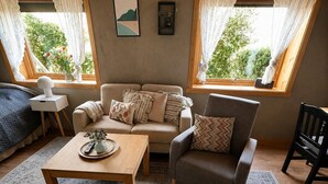 En hyggelig stue med sofa, lænestol, sofabord og to vinduer med gardiner.