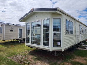 A mobile home with a large windowed front section, a nameplate, and a number sign.