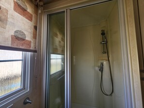 Eine Dusche mit Handbrause und Duschschlauch, ein Fenster mit Vorhang sowie eine Tür mit Griff.