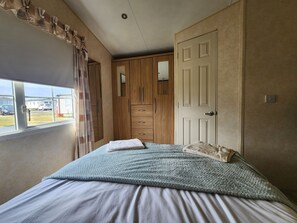 Ein Schlafzimmer mit Bett, Kleiderschrank, einem Fenster mit Vorhängen und Blick ins Freie.