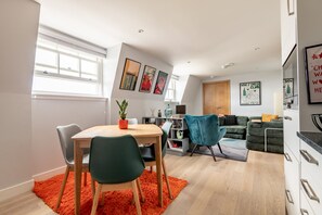 A modern apartment with a dining area, a living room, and a kitchen. There are framed pictures on the walls, a wooden dining table with chairs, and a sofa in the living room. - Century Court (No 10) | St Andrews (St Andrews)