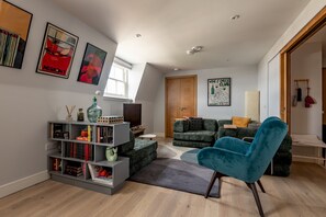 A modern living room with a bookshelf, a blue armchair, and a television. - Century Court (No 10) | St Andrews (St Andrews)