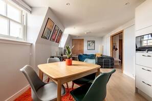 A modern kitchen with white cabinets, a built-in oven, and a dining area with a wooden table and chairs. - Century Court (No 10) | St Andrews (St Andrews)