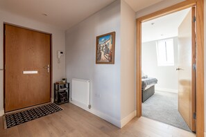 Passadís amb una porta de fusta, un radiador, un quadre i un visió d'una habitació amb un llit i una finestra.