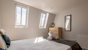 Une chambre à coucher avec un lit, deux fenêtres, une commode, un miroir et un radiateur.