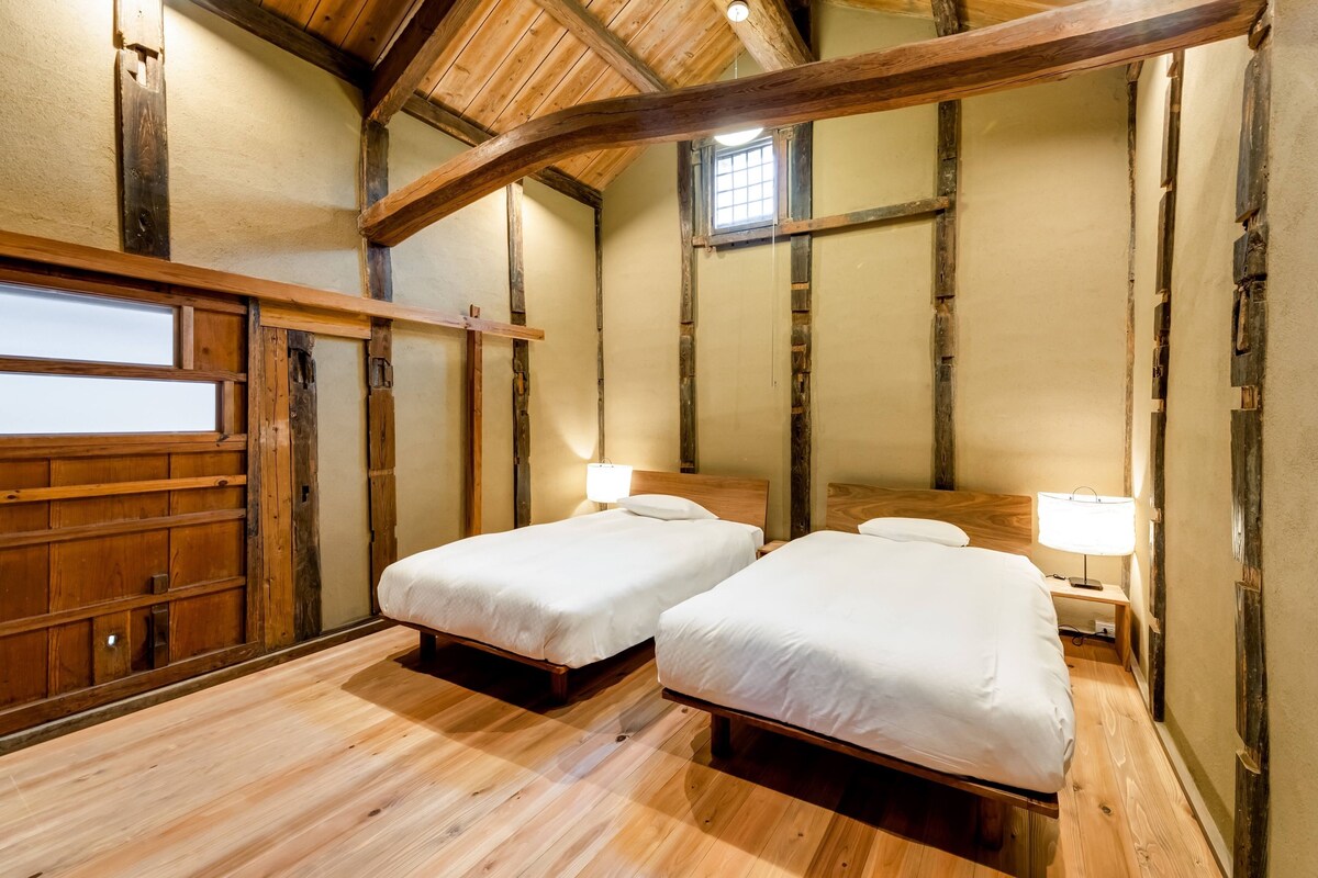 Una habitación con dos camas, vigas de madera, un ventanal y suelo de madera.