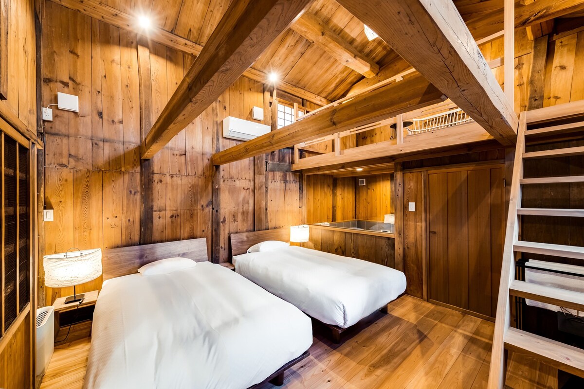 Una habitación tipo cabaña de madera con dos camas, un entrepiso y una pequeña cocina.