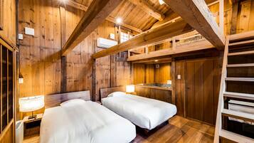 A wooden cabin room with two beds, a loft area, and a small kitchenette.