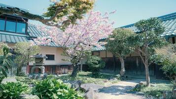 A traditional Japanese building with a tiled roof, surrounded by a garden with cherry blossoms and a stone lantern.
