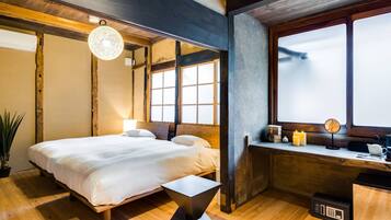 A bedroom with a bed, bedside table, window, and a small desk area with a lamp and candles.