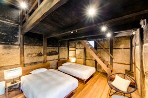 Una habitación rústica con vigas de madera, dos camas, una silla y una escalera.