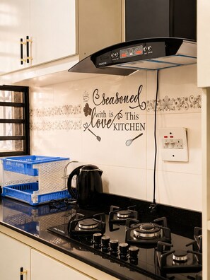 Eine Küche mit Herd, Wasserkocher und einer Wand mit einer dekorativen Fliese, auf der steht: 'Seasoned with love This kitchen'.