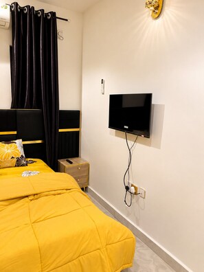 Ein Schlafzimmer mit einem Bett, einem an der Wand montierten Fernseher und einem Nachttisch.