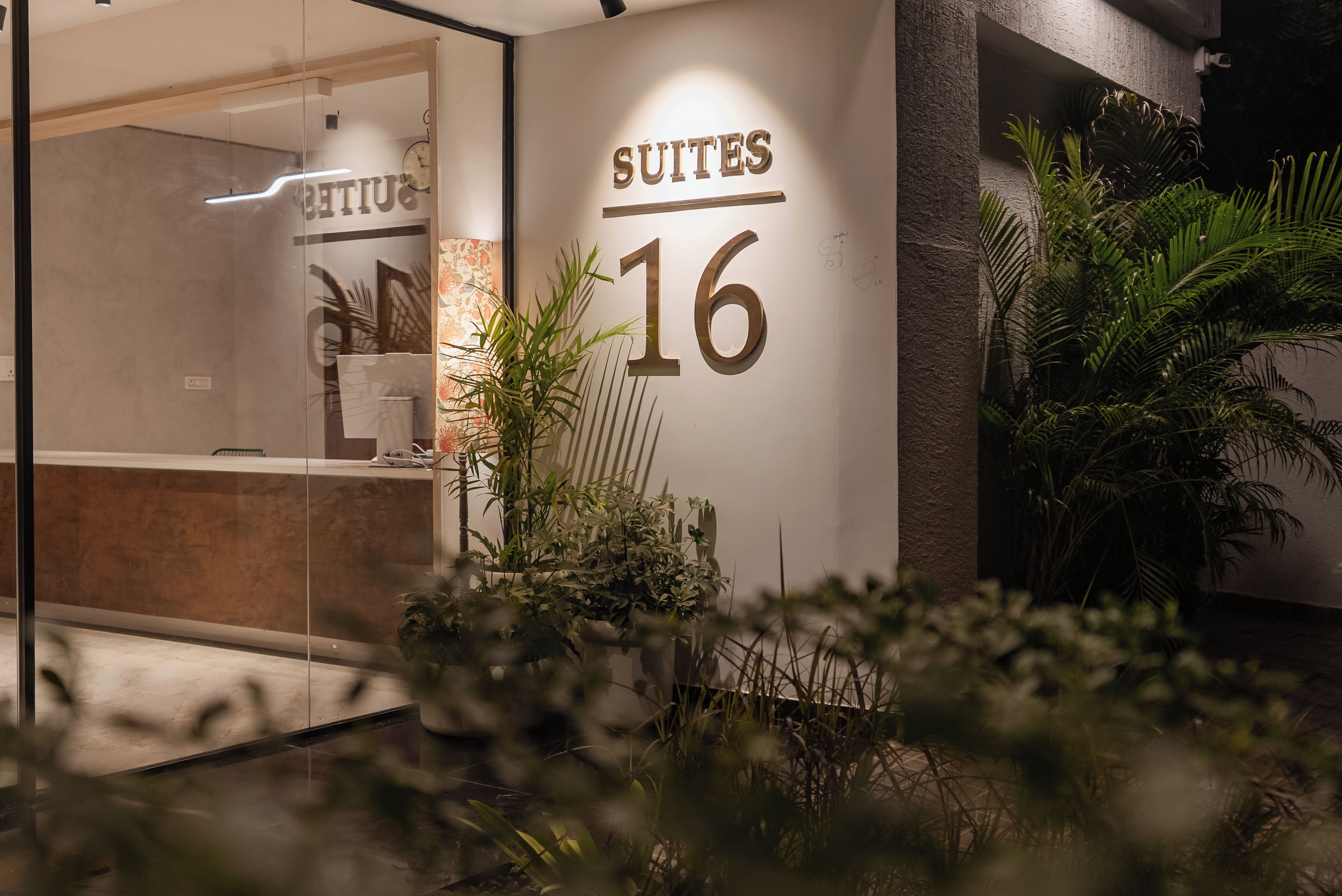 L'ingresso di un hotel con una reception, un cartello che indica 'Suites 16' e piante da interno.
