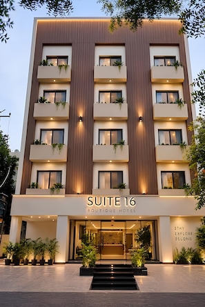 Un moderno edificio de hotel con un cartel que dice 'SUITE 16 BOUTIQUE HOTEL' y una entrada acogedora con escalones y plantas en macetas.
