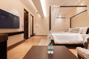 Un dormitorio moderno con una televisión de pantalla plana, una cama con ropa de cama blanca, una mesita de noche con botellas de agua y un suelo de madera.
